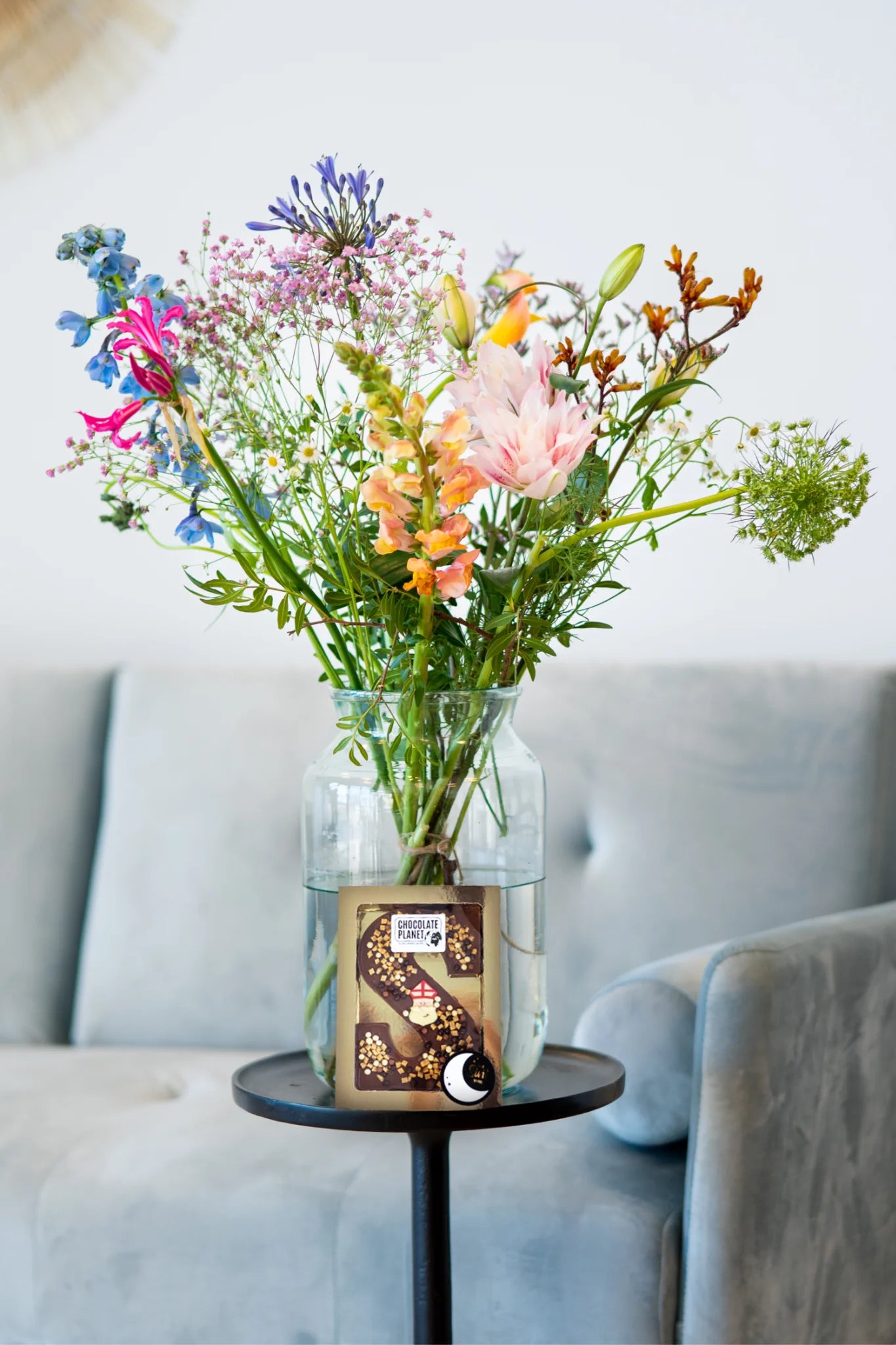Een kleurrijk boeket met diverse bloemen in een glazen vaas, vergezeld door een chocoladeletter van Sint
