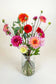 Biologisch boeket dahlia's in glazen vaas met rode, oranje, roze en magenta bloemen