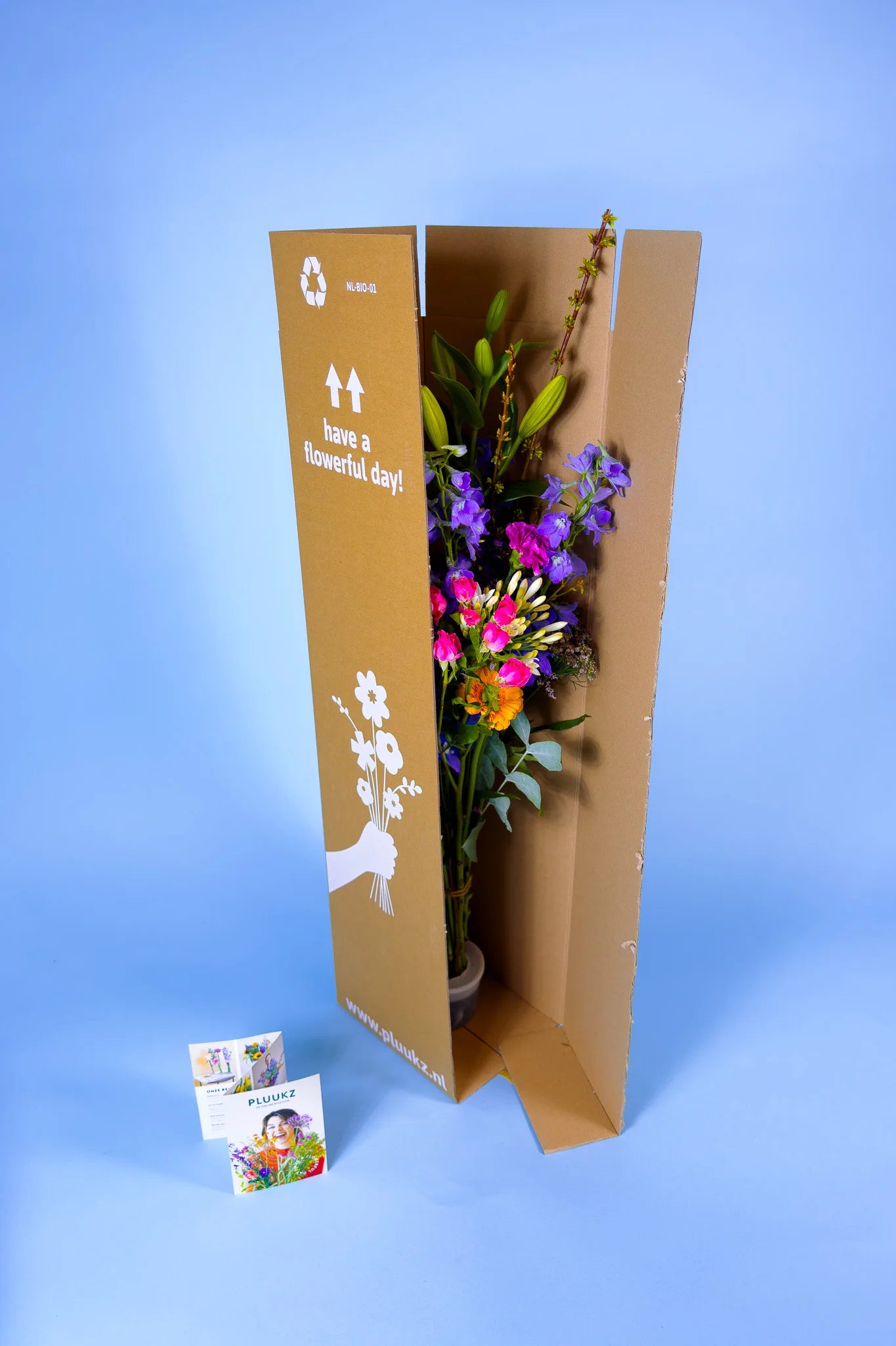 Een Pluukz boeket met diverse bloemen staat in een hoge, bruine Pluukz verzenddoos.